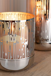 Nahaufnahme eines eleganten Windlichts mit geometrischem Muster und glänzender Oberfläche, das auf einem Holztisch steht.