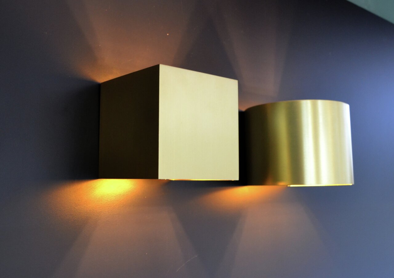 Lucide Wandleuchte XIO Moderne Wandleuchte XIO in goldener Farbe, seitliche Perspektive, mit warmem Lichtschein nach oben und unten.