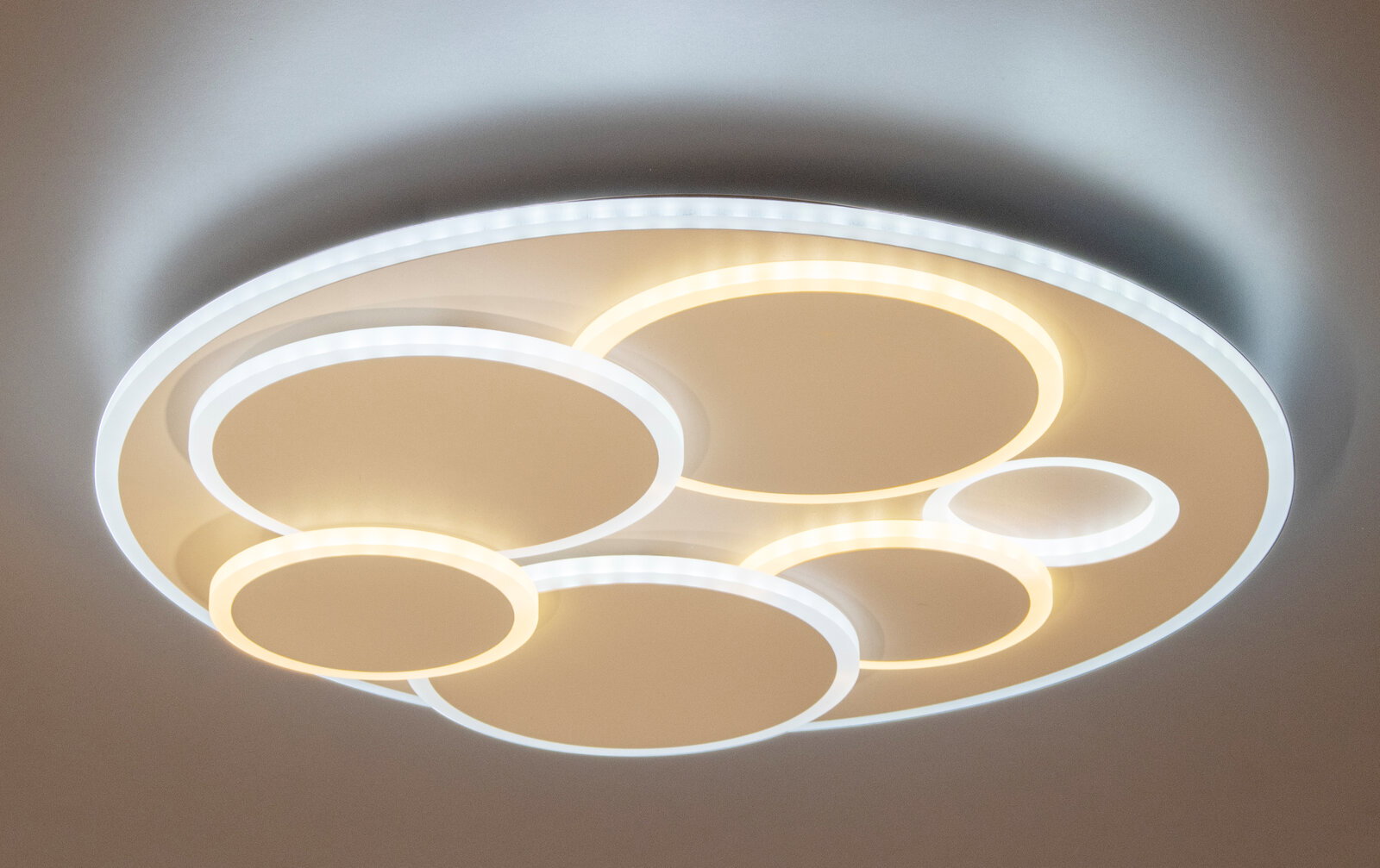 Moderne runde LED-Deckenleuchte mit mehreren überlappenden Leuchtringen in Warmweiß und Kaltweiß, Ansicht von unten an der Decke