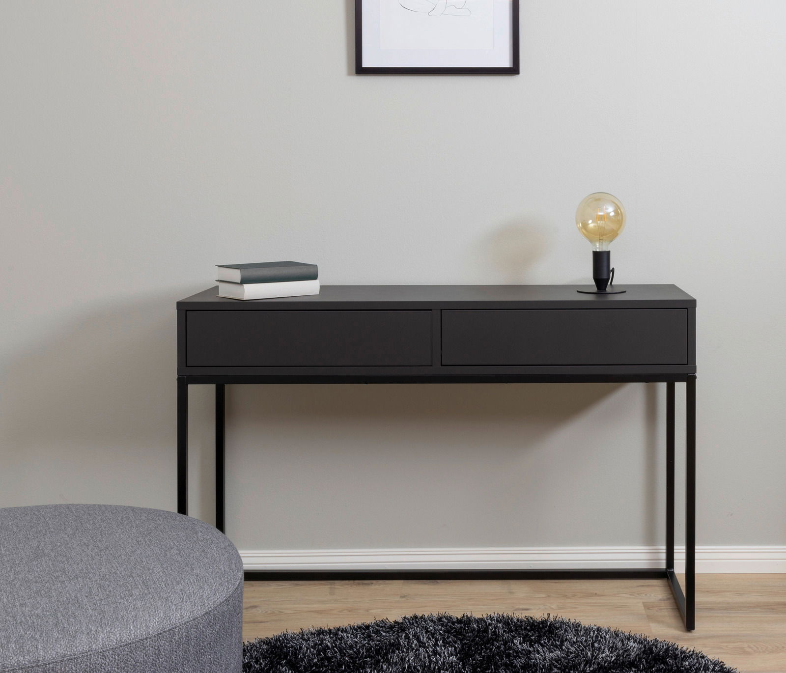 Schwarze Konsole mit zwei Schubladen, darauf eine Lampe und Bücher, aus frontaler Perspektive fotografiert.