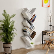 Modernes weißes Zickzack-Standregal/Bücherregal mit mehreren schrägen Fächern, gefüllt mit Büchern, in einem hellen Wohnzimmer neben Zimmerpflanze und Beistelltisch; Frontansicht in leichter Schrägperspektive von links.