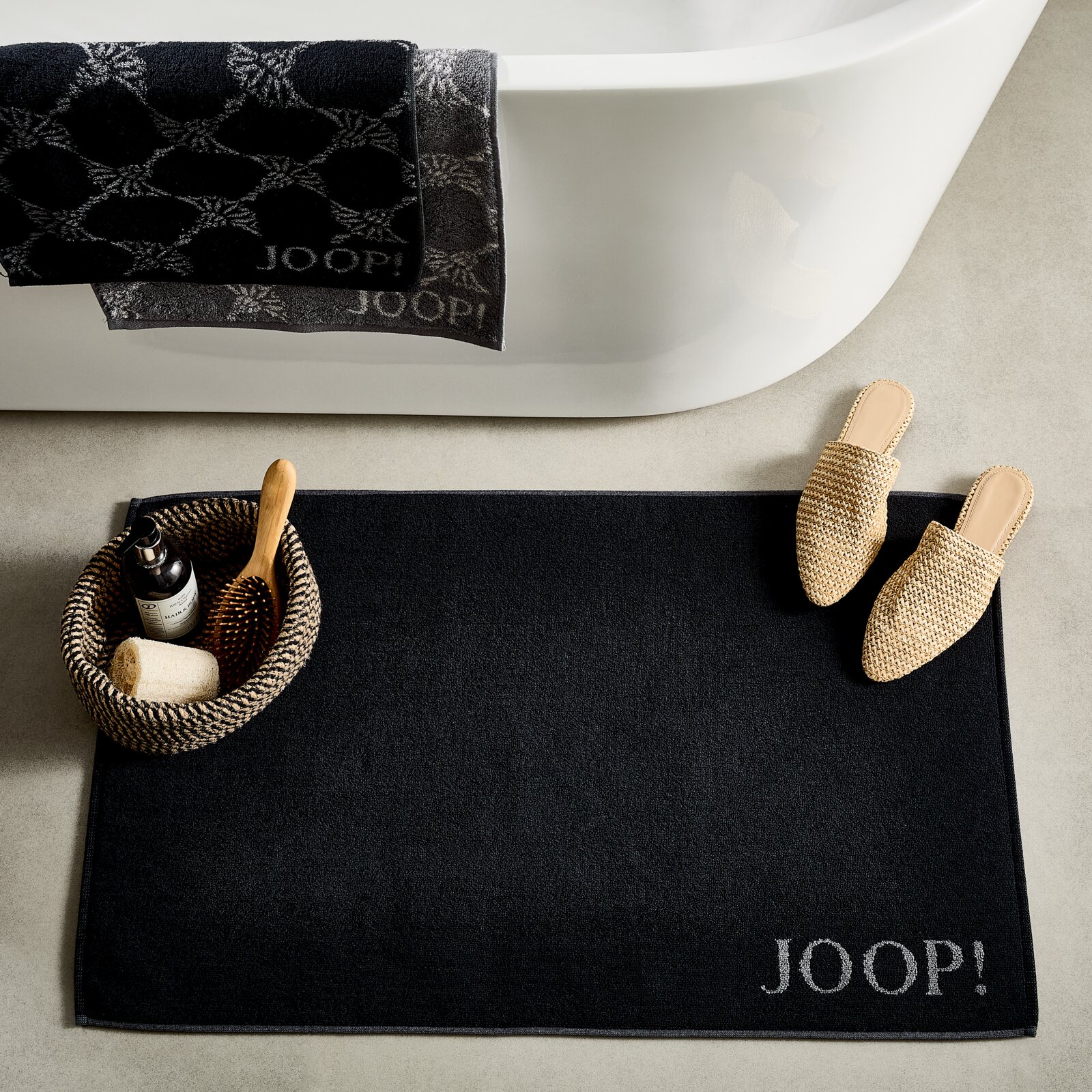 JOOP! Badmat DOUBLEFACE JOOP! Badmat DOUBLEFACE in zwart, gefotografeerd van bovenaf, naast een badkuip met handdoeken en een mand met verzorgingsproducten.