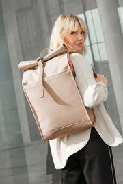 Frau mit beigem Rolltop-Rucksack in urbaner Umgebung, seitliche Perspektive