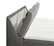 Seitliche Ansicht eines grauen Boxspringbetts mit geöffnetem Stauraum und weißer Matratze.