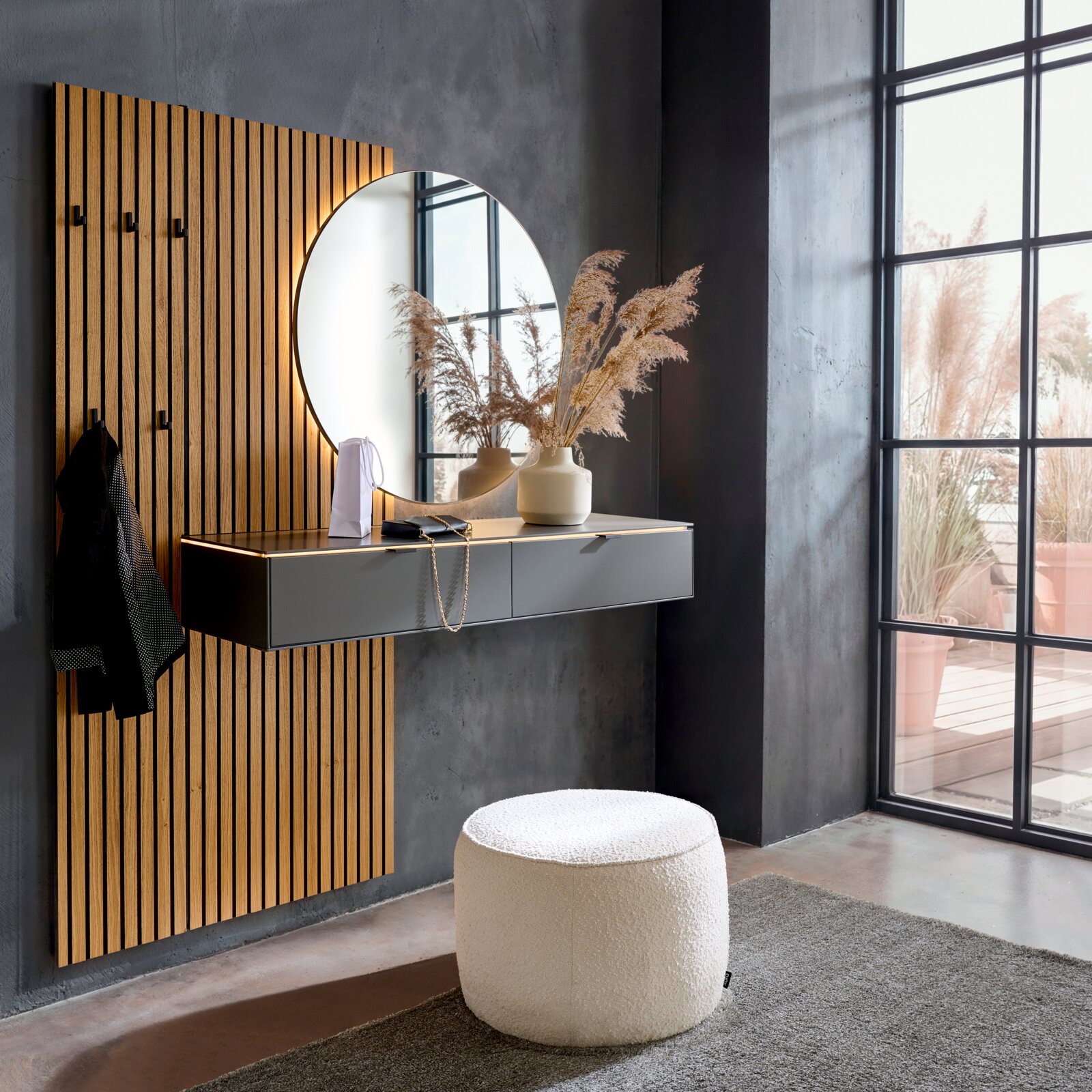 Modernes Eingangs-Set mit vertikaler Holz-Lamellenpaneel-Garderobe, rundem Wandspiegel mit indirekter Beleuchtung und schwebender grauer Konsole mit Schubladen; Perspektive: leicht schräg von vorn links im Raum aufgenommen.