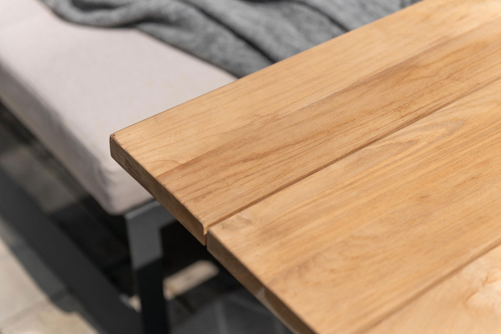 Nahaufnahme eines Gartentisches aus Holz mit einer Sitzbank im Hintergrund, Perspektive von oben.