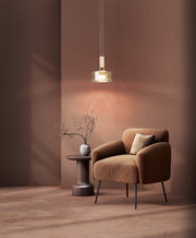 Moderne Pendelleuchte mit zylindrischem Glasschirm und warmem Licht über einem braunen Sessel neben einem Beistelltisch mit Vase, frontale leicht seitliche Perspektive