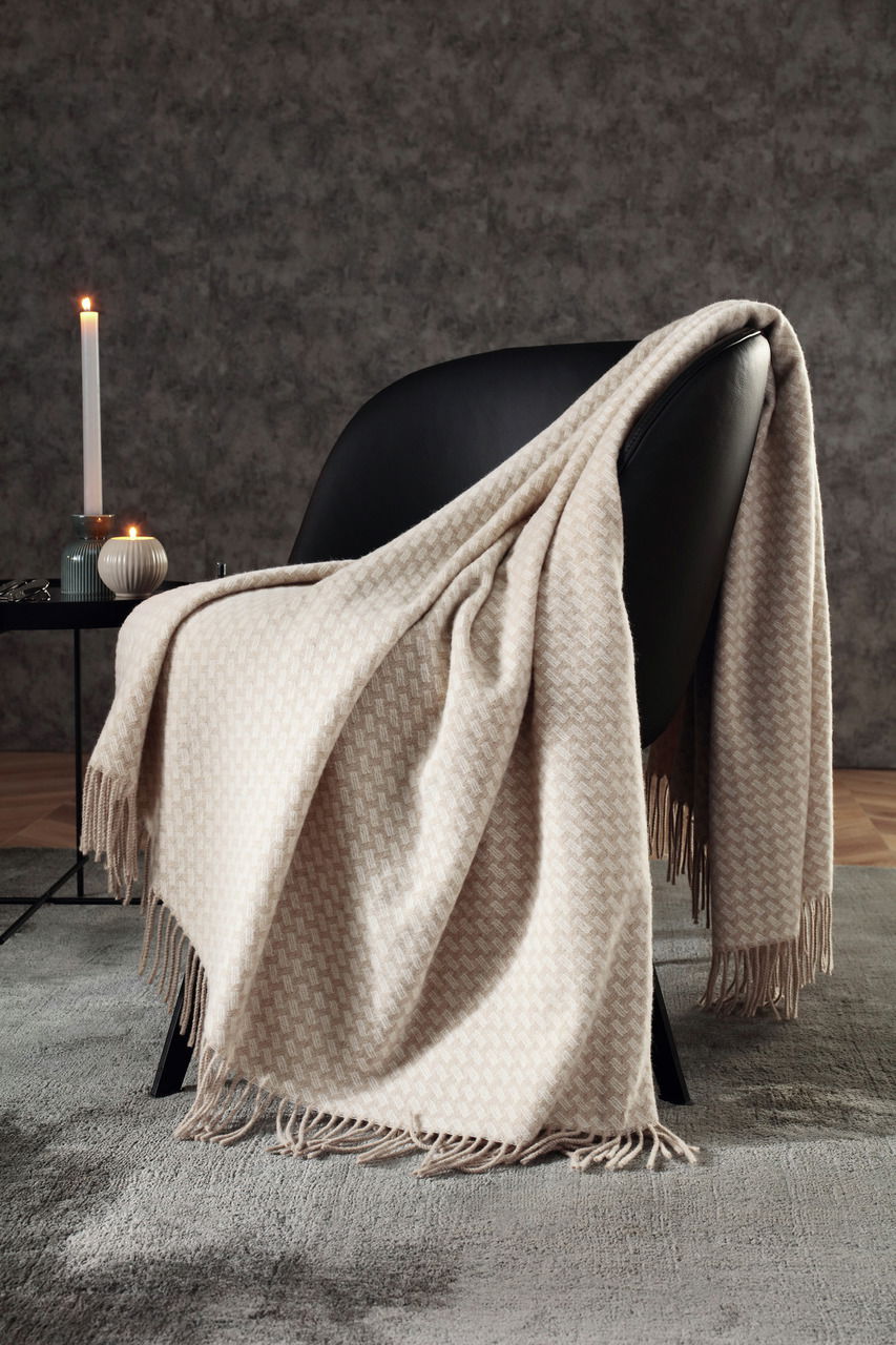 Beige gemusterte Decke mit Fransen, drapiert über einem schwarzen Stuhl in einem stilvollen Wohnzimmer, seitliche Perspektive.