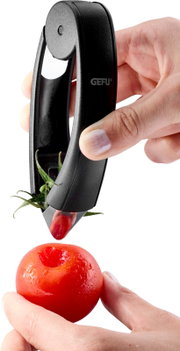 Zwarte GEFU tomatenontkroner in gebruik: hand verwijdert het kroontje van een rode tomaat, close-up vanuit zijaanzicht