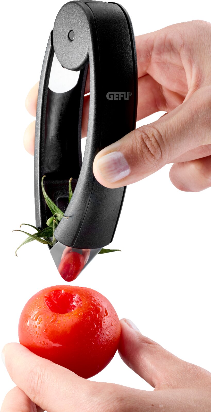 Zwarte GEFU tomatenontkroner in gebruik: hand verwijdert het kroontje van een rode tomaat, close-up vanuit zijaanzicht