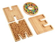 Servierbretter aus Bambus in der Form der Buchstaben H, O, M, E, gefüllt mit bunten Süßigkeiten und Brezeln, aus der Vogelperspektive.