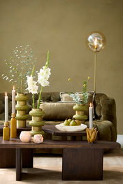 Moderner Couchtisch aus dunklem Holz mit dekorativen Vasen und Kerzen, im Hintergrund ein grünes Sofa und eine Stehlampe. Perspektive: Frontalansicht.