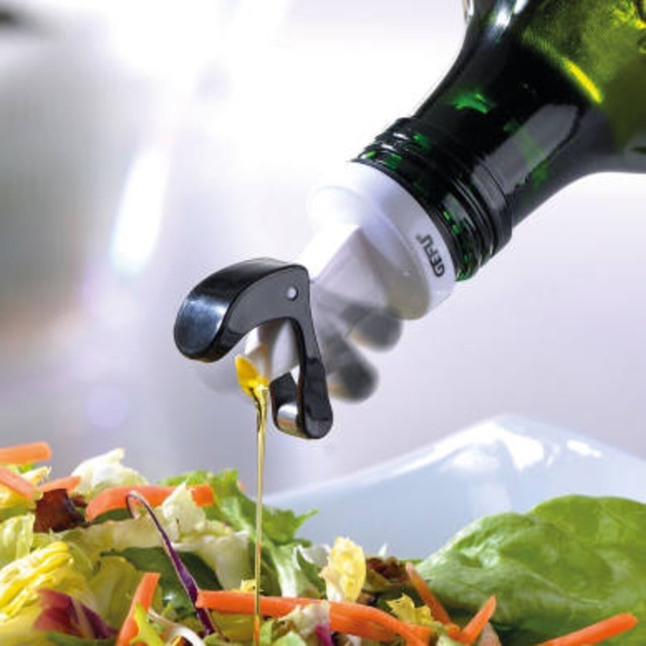 Ausgießer AUTOMATICO in Aktion, seitliche Perspektive, gießt Öl über einen frischen Salat.