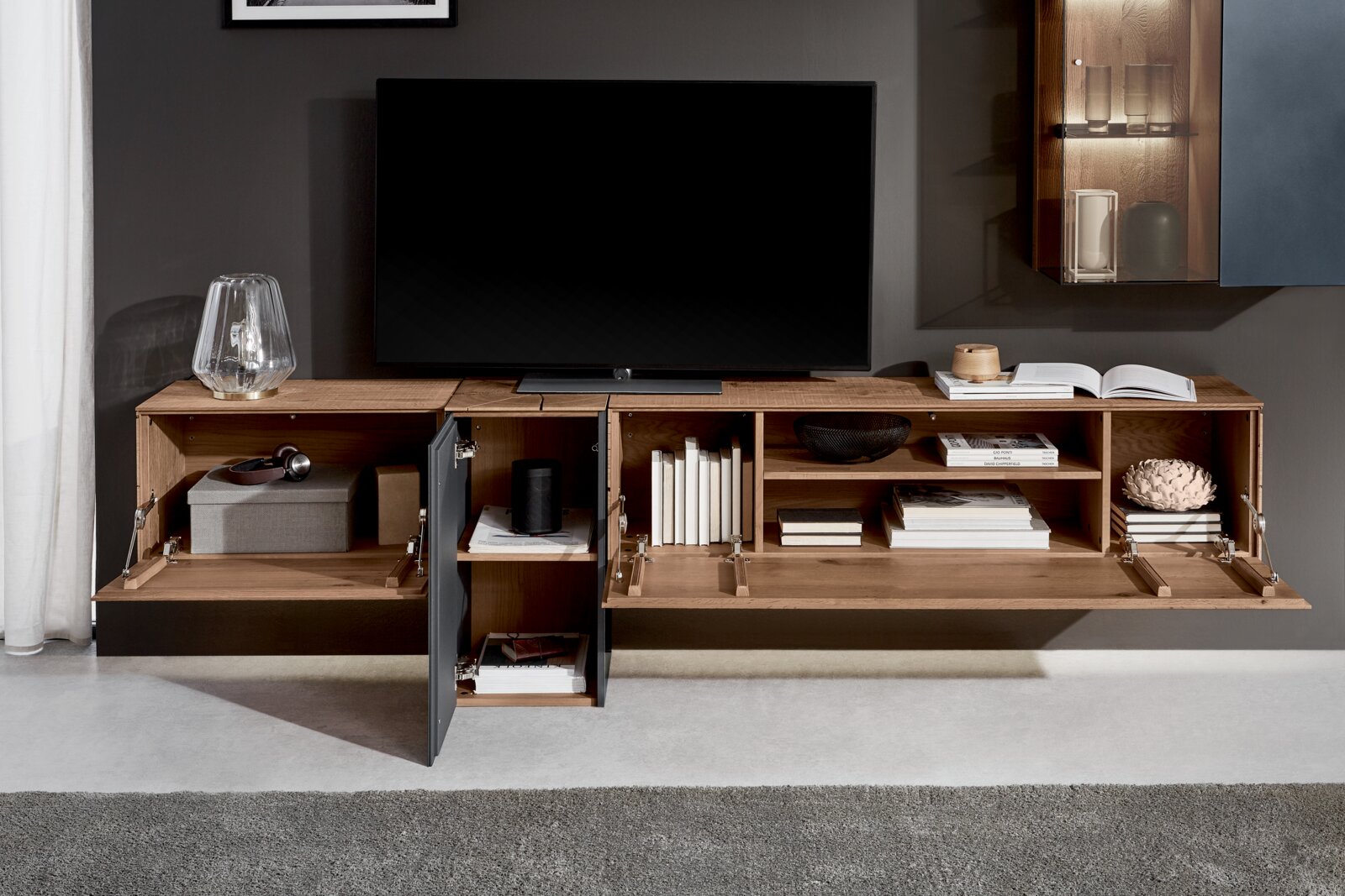 Moderne wandcombinatie van hout met open en gesloten vakken, versierd met boeken en accessoires, gezien vanaf de voorkant.