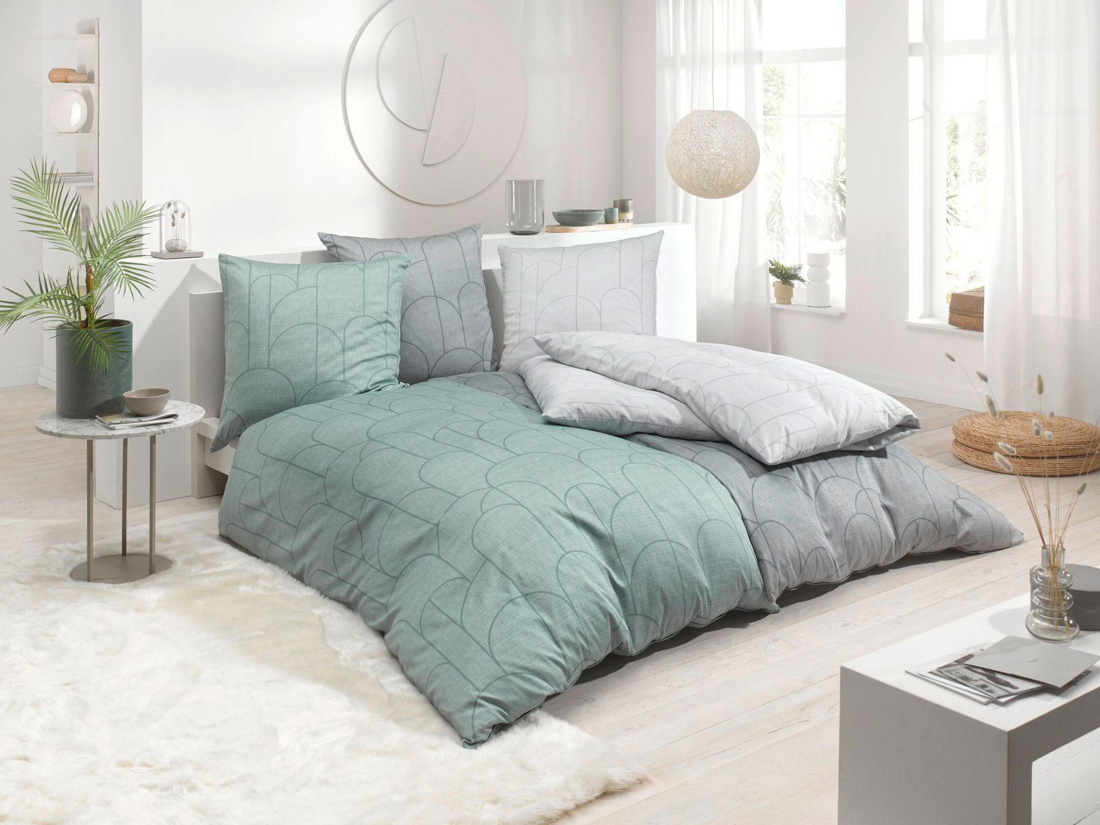 Bettwäsche-Set in einem modernen Schlafzimmer mit Tageslicht, bestehend aus Kissen und Decken in Grün- und Grautönen mit geometrischem Muster, seitliche Perspektive.