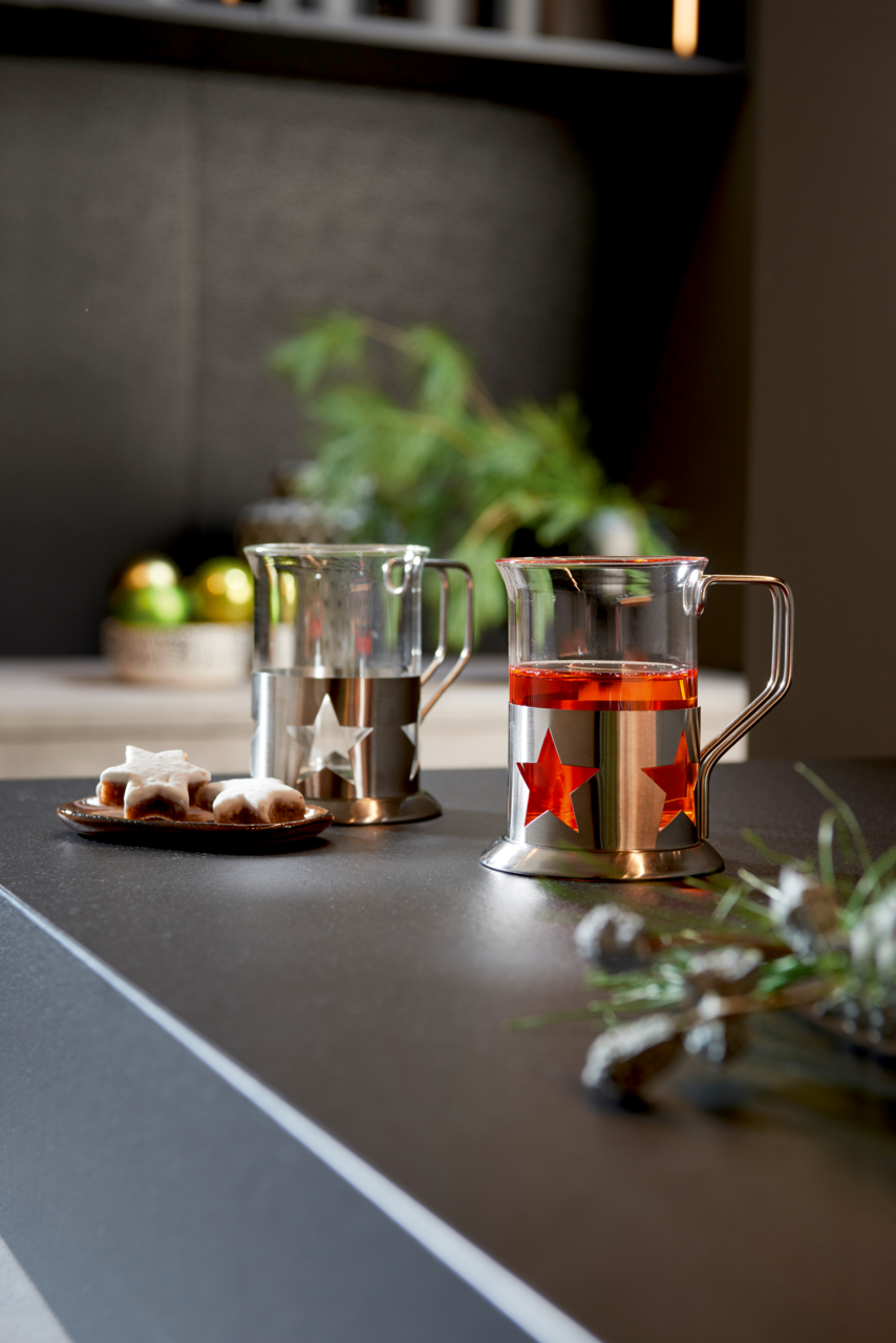 Leonardo Teegläser 2er-Set Zwei Teegläser mit Sternendesign aus Metall, eines mit rotem Tee gefüllt, auf einer Küchenarbeitsplatte. Seitliche Perspektive.