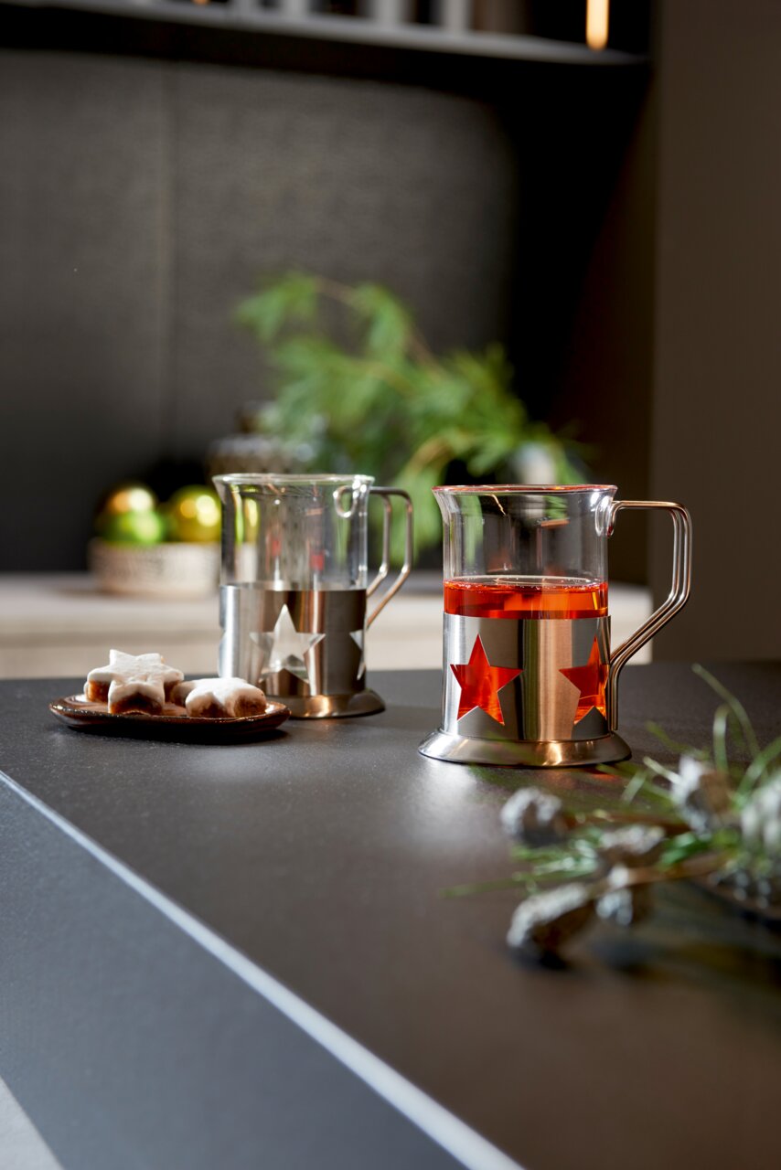 Leonardo Teegläser 2er-Set Zwei Teegläser mit Sternendesign aus Metall, eines mit rotem Tee gefüllt, auf einer Küchenarbeitsplatte. Seitliche Perspektive.
