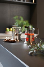 Zwei Teegläser mit Sternendesign aus Metall, eines mit rotem Tee gefüllt, auf einer Küchenarbeitsplatte. Seitliche Perspektive.