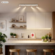 Moderne weiße Decken-Spotleiste mit vier verstellbaren Strahlern und warmem Licht über einer minimalistischen Küche, Ansicht leicht von unten/Frontansicht.