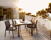Moderner Gartentisch mit vier Stühlen auf einer Terrasse, umgeben von Bäumen und Sonnenlicht, seitliche Perspektive.