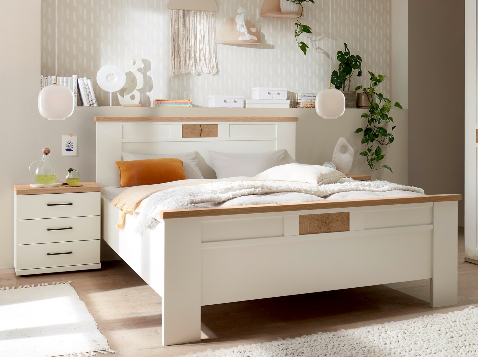 Modernes Doppelbett in Weiß mit Holz-Akzenten, bezogen mit weißer Bettwäsche und orangefarbenem Kissen, im hellen Schlafzimmer mit Nachttisch und Deko, Frontansicht in leichter Schrägperspektive von vorn links