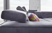 Nahaufnahme eines modernen Ecksofas in Grau mit verstellbarer Kopfstütze und buntem Kissen, seitliche Perspektive.