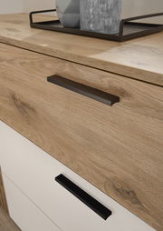 Nahaufnahme einer Kommode mit Holzoptik und modernen schwarzen Griffen, von schräg oben fotografiert.