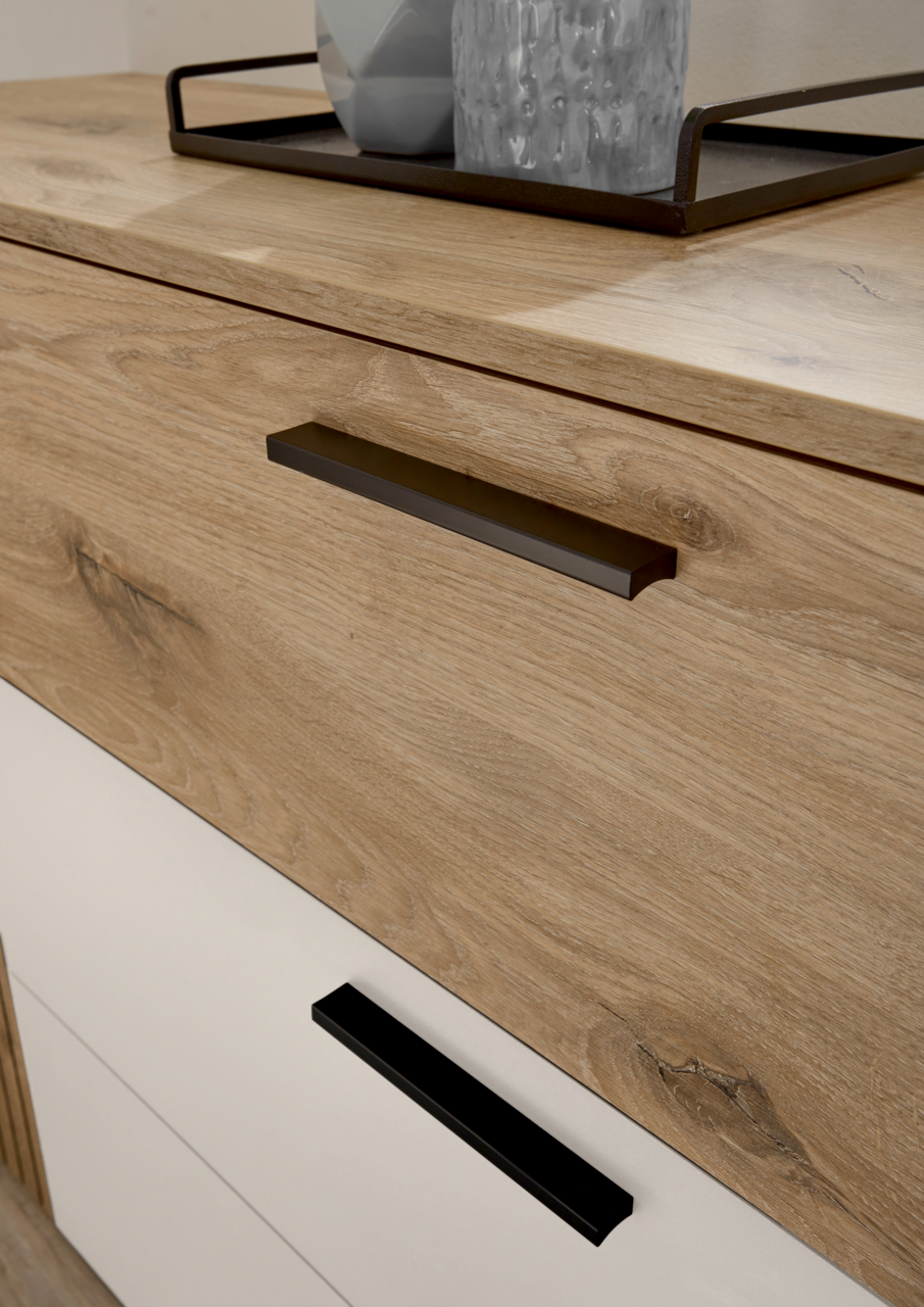 Nahaufnahme einer Kommode mit Holzoptik und modernen schwarzen Griffen, von schräg oben fotografiert.