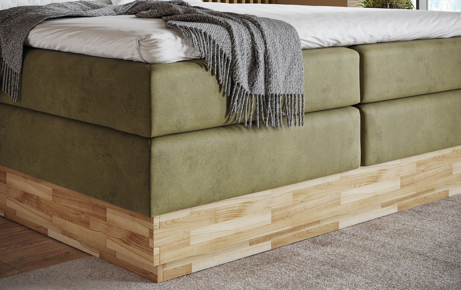 Nahaufnahme eines Boxspringbetts mit olivgrünem Stoffbezug und Holzunterbau, seitliche Perspektive