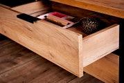 Nahaufnahme einer geöffneten Schublade eines Eck-Schreibtisches aus Holz mit schwarzem Griff, gefüllt mit Schreibutensilien und einer Schnurrolle.