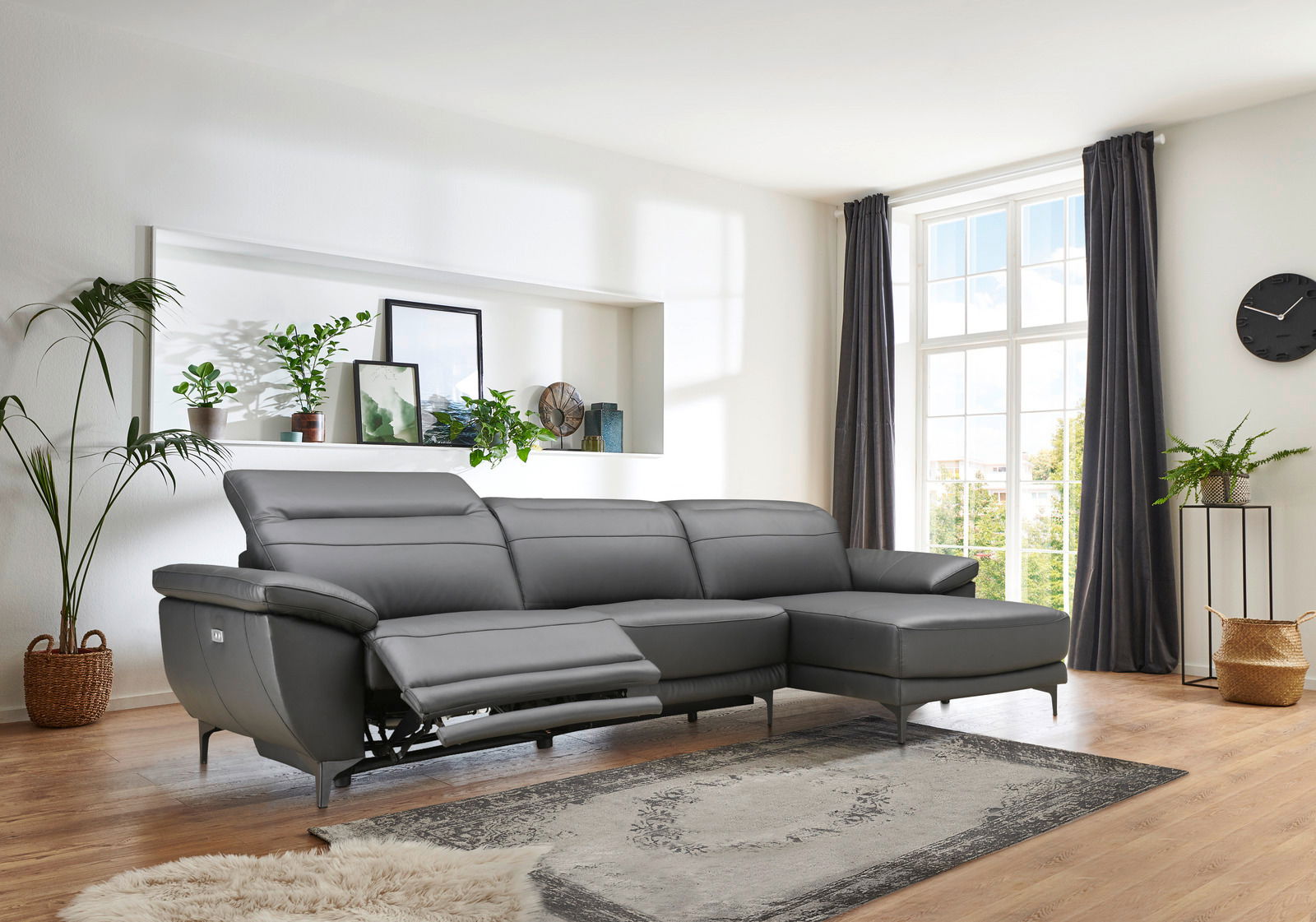 Graue Longchairkombination RONALD von XORA in einem modernen Wohnzimmer, seitliche Perspektive mit Blick auf das Sofa und die Fenster im Hintergrund.