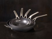 Ein Stapel von Bratpfannen der Serie Raise in verschiedenen Größen, von der Seite betrachtet, mit Edelstahlgriffen.