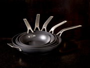 Ein Stapel von Bratpfannen der Serie Raise in verschiedenen Größen, von der Seite betrachtet, mit Edelstahlgriffen.