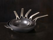 Ein Stapel von Bratpfannen der Serie Raise in verschiedenen Größen, von der Seite betrachtet, mit Edelstahlgriffen.