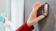 Nahaufnahme einer Hand, die einen Edelstahlhaken an einer grauen Wand im Badezimmer anbringt.