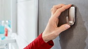 Nahaufnahme einer Hand, die einen Edelstahlhaken an einer grauen Wand im Badezimmer anbringt.