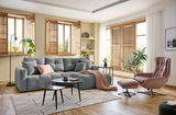 Gemütliche Wohnzimmer-Ecke mit grauem Rundecksofa, dekoriert mit Kissen und Decke, aus der Perspektive von vorne.
