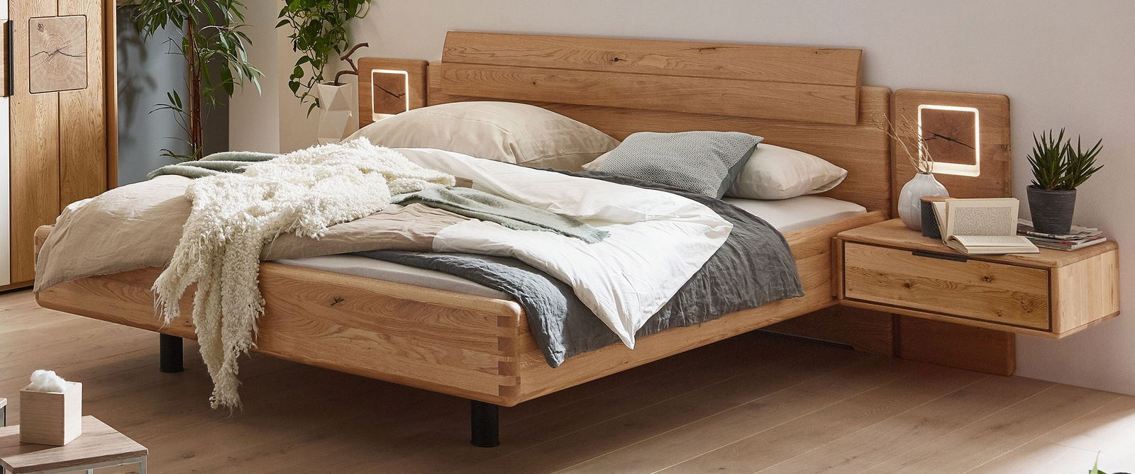 Holz-Nachtkonsole rechts neben einem Bett, mit moderner Beleuchtung und Dekoration, aus der Perspektive von vorne rechts.