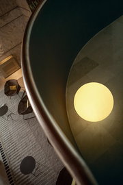 Blick von oben in ein modernes Atrium mit runder, warm leuchtender Deckenlampe und Sitzgruppe im unteren Bereich