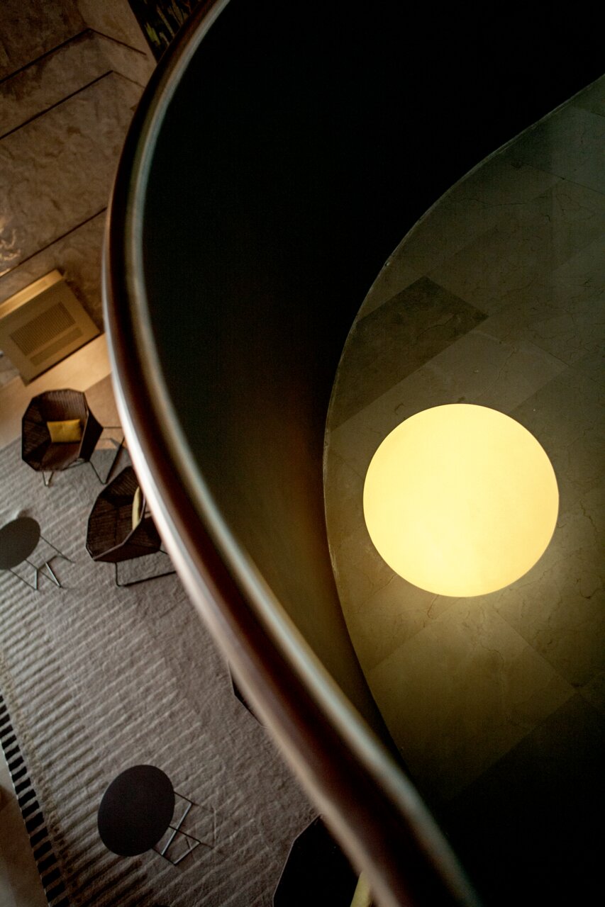 Bovenaanzicht van een modern atrium met een ronde, warm verlichtende plafondlamp en een zithoek in het lagere gedeelte