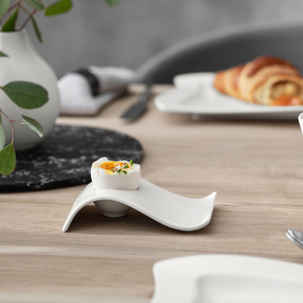 Moderner Eierbecher NewWave aus weißem Porzellan mit geschwungenem Design, seitliche Perspektive auf einem gedeckten Tisch.
