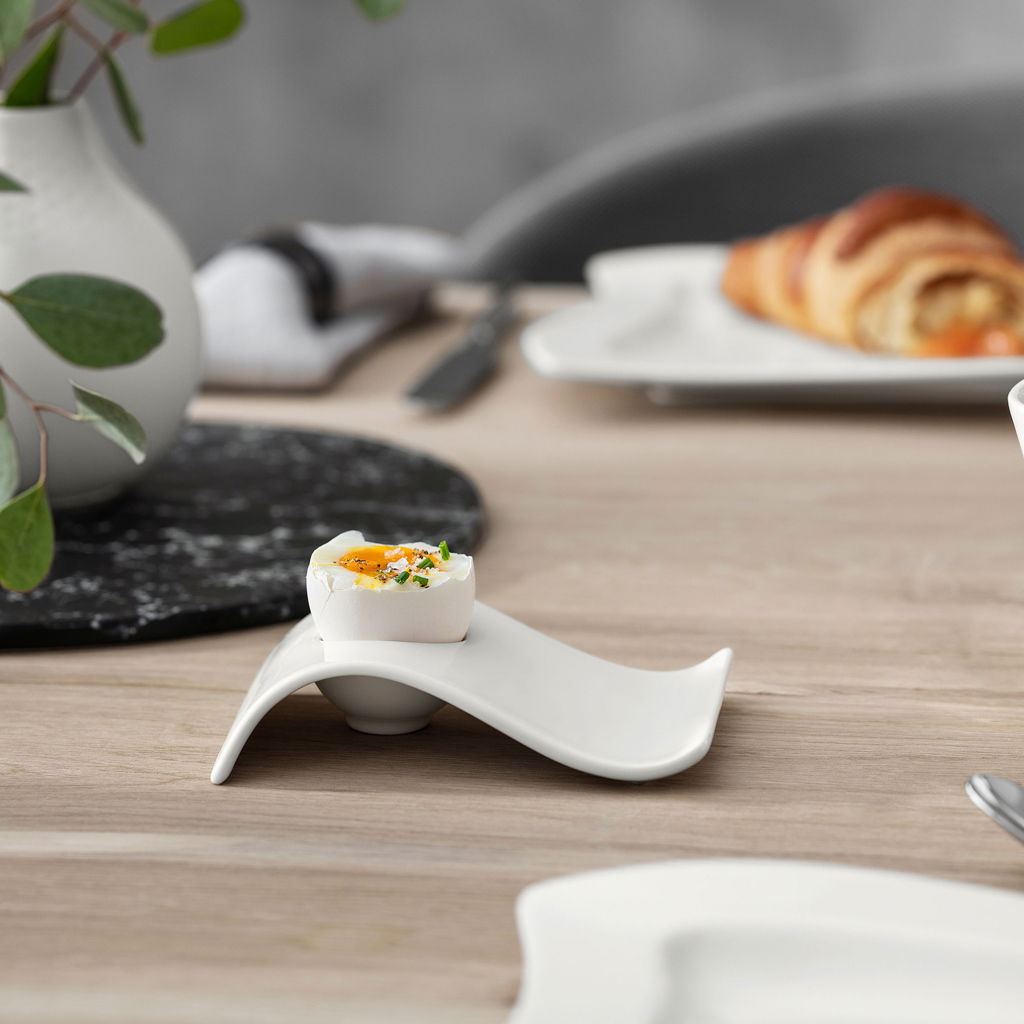 Moderner Eierbecher NewWave aus weißem Porzellan mit geschwungenem Design, seitliche Perspektive auf einem gedeckten Tisch.