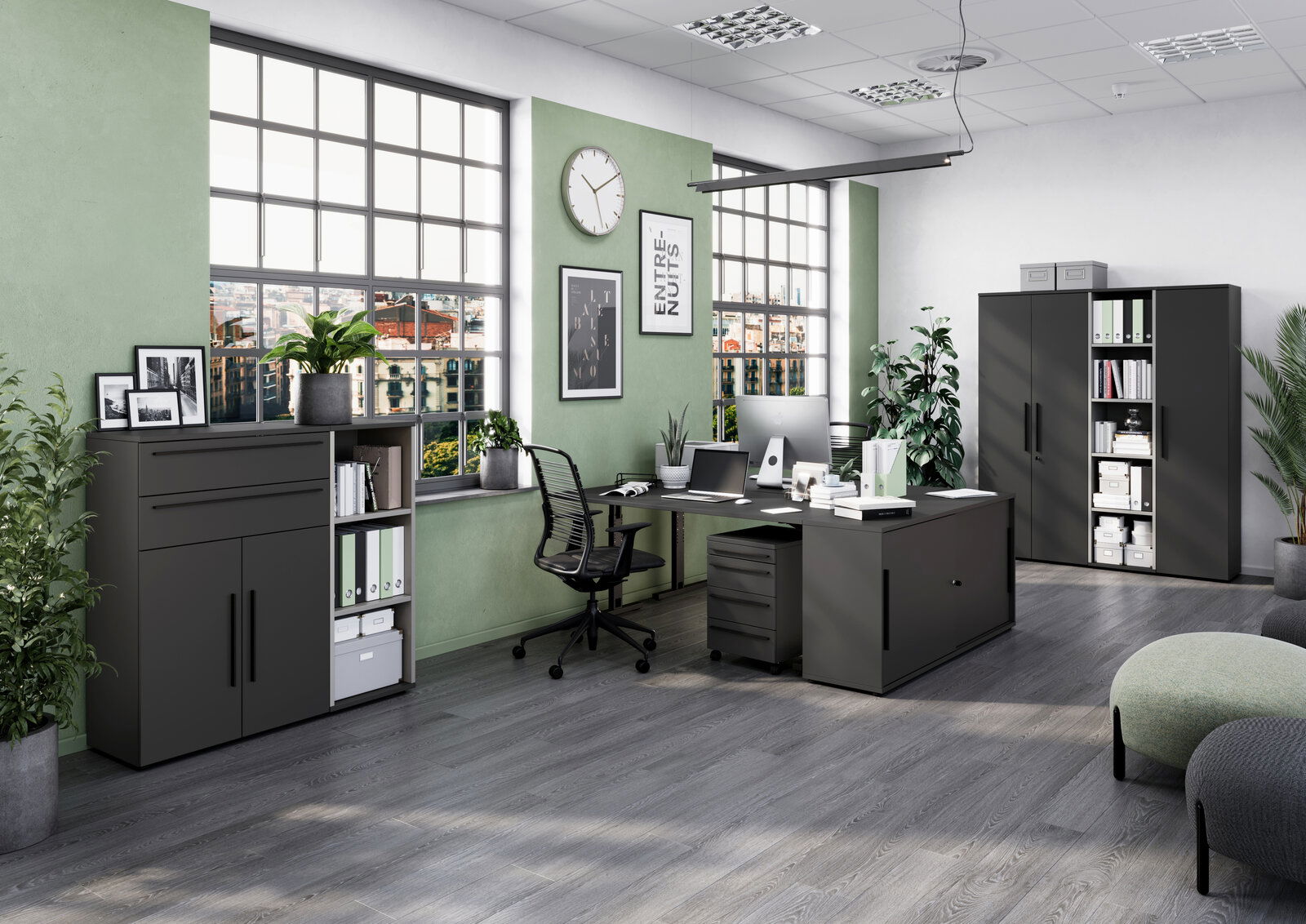 Moderne Büroeinrichtung mit Winkelschreibtisch, Rollcontainer und Aktenschränken in einem hellen Raum mit großen Fenstern und grünen Wänden. Perspektive von vorne links.