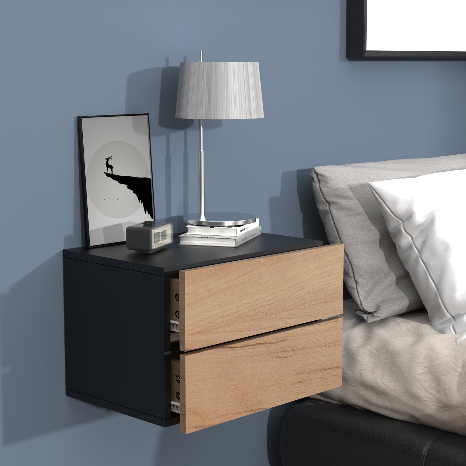 Wandmontierter Nachttisch in Schwarz mit zwei Holz-Schubladen neben einem Bett, darauf eine silberne Tischlampe, Bücher und ein gerahmtes Bild Ansicht schräg von vorn rechts