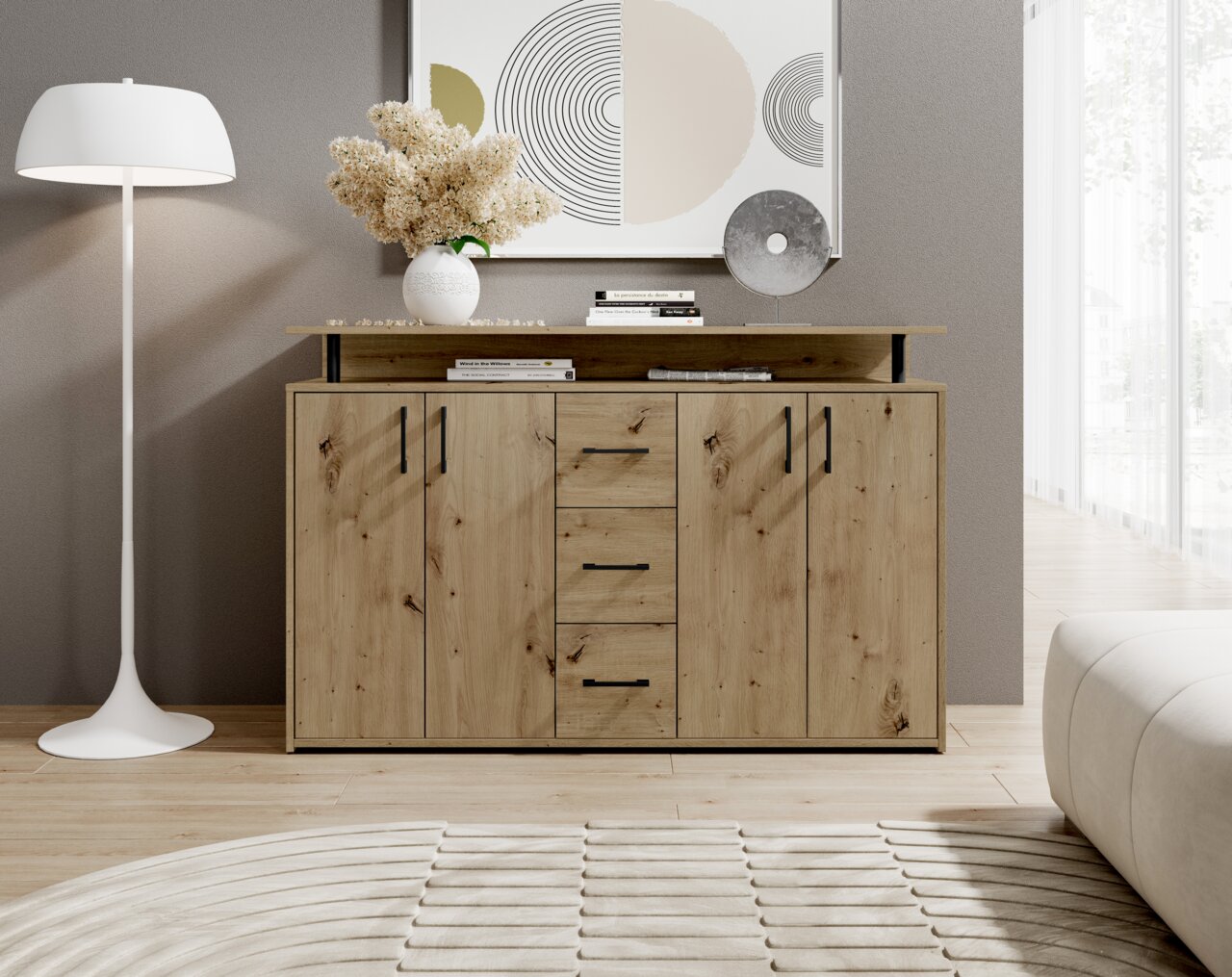 Vooraanzicht van een modern houten dressoir met vier lades en twee deuren, versierd met boeken en een vaas met bloemen, naast een staande lamp in een stijlvolle woonkamer.