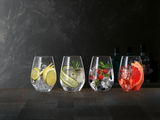 Vier Gin Tonic Gläser auf einem Tisch, gefüllt mit Eis und verschiedenen Zutaten wie Limetten, Gurken, Beeren und Grapefruit, aus frontaler Perspektive fotografiert.