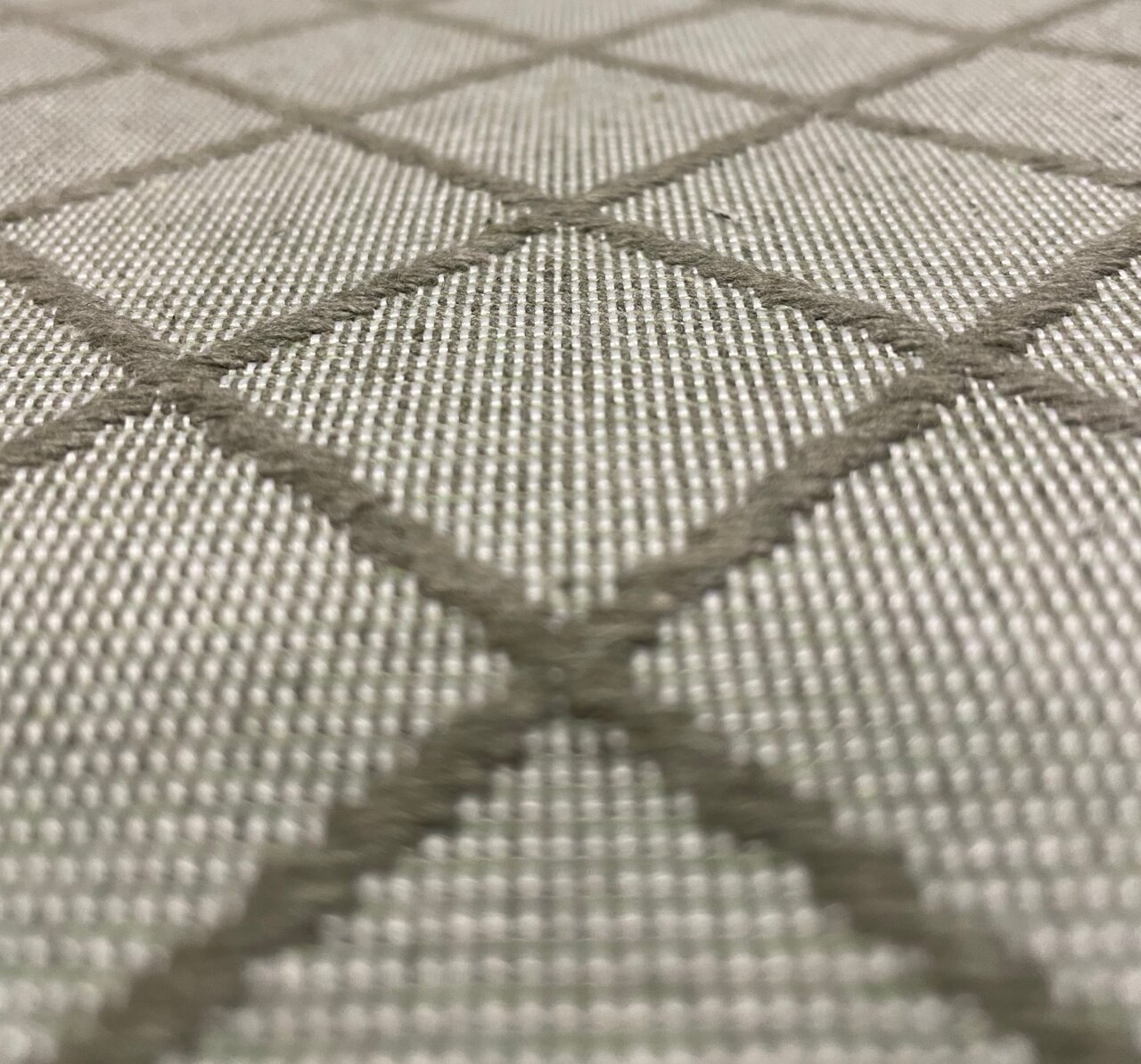 Nahaufnahme eines Stoffmusters mit grauem Rautenmuster, perspektivisch von der Seite aufgenommen.