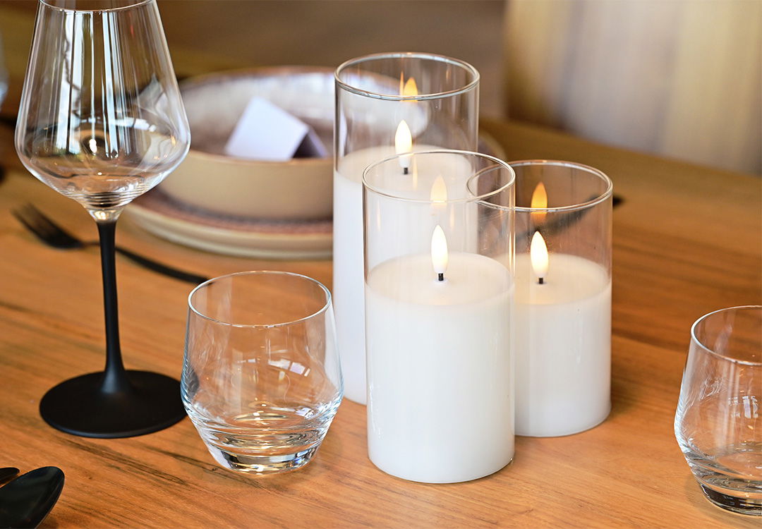 Drei weiße LED-Kerzen in Glaszylindern auf Holztisch, sorgen für einestimmungsvolle Tischbeleuchtung