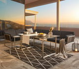 Moderne Loungegarnitur auf Terrasse mit Meerblick bei Sonnenuntergang, bestehend aus einem großen Loungetisch, zwei Loungesesseln und einem Ecksofa, aus seitlicher Perspektive fotografiert.