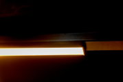 Close-up zijaanzicht van een slanke, rechthoekige LED-lichtbalk/armatuur met warmwit licht in een donkere omgeving